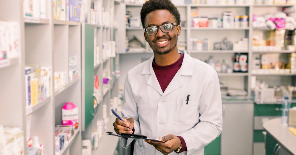 young african american male pharmacist writing on clipboard while working at pharmacy
