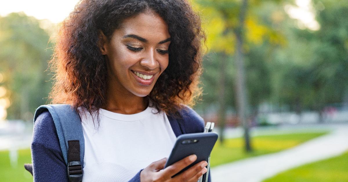 African woman student walking in the park chatting by mobile phone