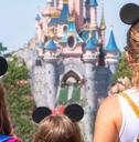 A mother and her daughters gaze at the Princess Castle in a Disney park.