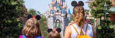 A mother and her daughters gaze at the Princess Castle in a Disney park.