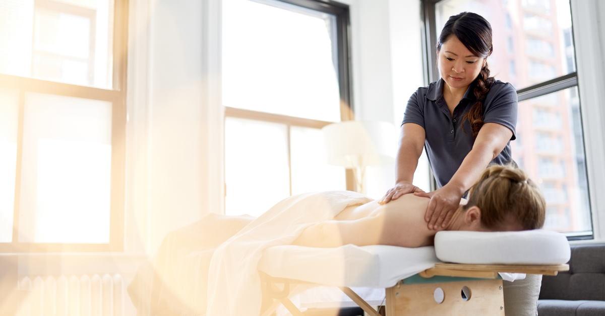 female asian therapist giving massage to young girl lying over massage bed