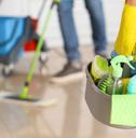 Female janitor holding a basket of cleaning supplies in the foreground with another janitor mopping in the background.l