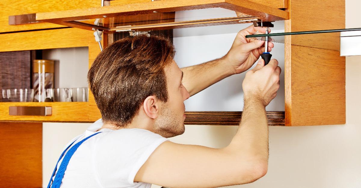 Handyman fixing kitchen's cabinet with screwdriver