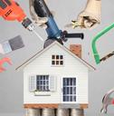 Hands holding up various tools, such as a drill and a paintbrush, around a model of a house that&#x27;s sitting on stacks of quarters.