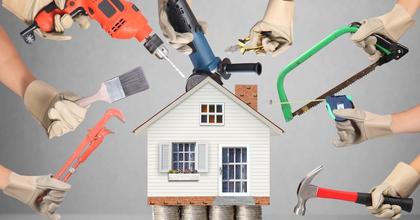Hands holding up various tools, such as a drill and a paintbrush, around a model of a house that&#x27;s sitting on stacks of quarters.