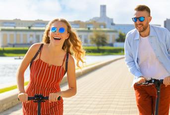 A couple having fun driving electric scooters along a city promenade.