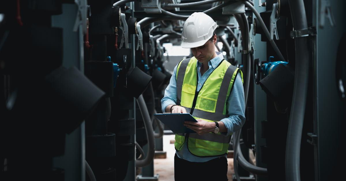 male engineer inspecting huge air conditioning unit while holding checklist on clipboard in hand