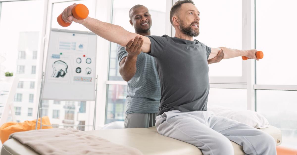 african american physiotherapist guiding young man to workout while holding his shoulders