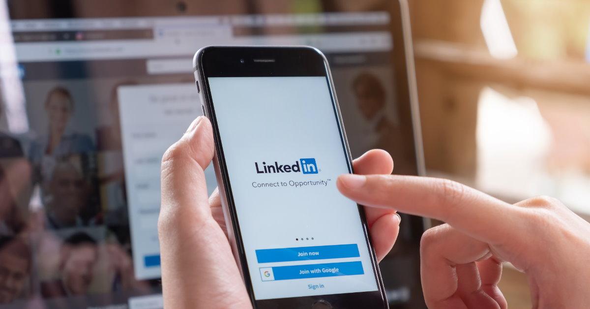 man using linkedin on mobile with laptop in background 