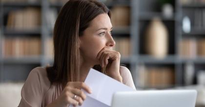Stressed young woman holding paper document, bank debt notification, looking away.