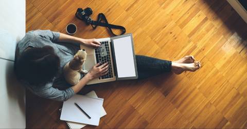 Woman sitting on the floor with her dog holding a credit card and laptop