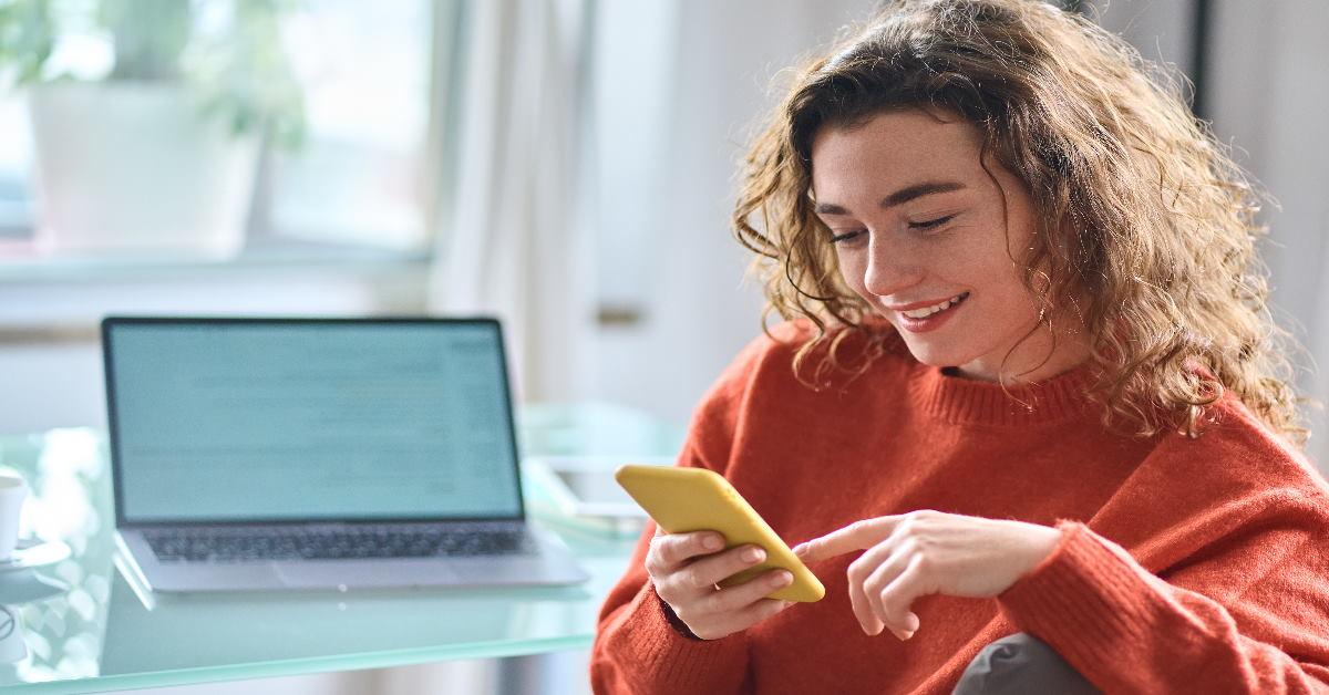 woman smiling at phone in front of laptop on table