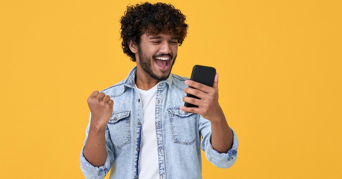 young indian man winner feeling joy using smartphone winning lottery game