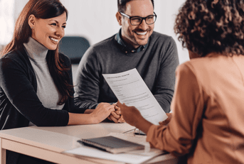 A couple holds hands and talks with a bank manager. 
