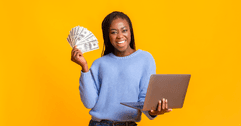 A woman holds a laptop in one hand and fans cash in the other. 