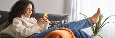 Smiling woman sitting on a couch and using a phone